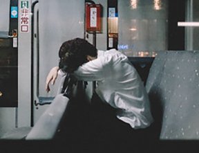 Image: tired man resting head on bent knees